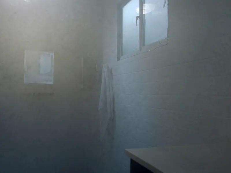 A steamed up bathroom with a white towel on a hook, a small window and a fogged mirror on tiled walls