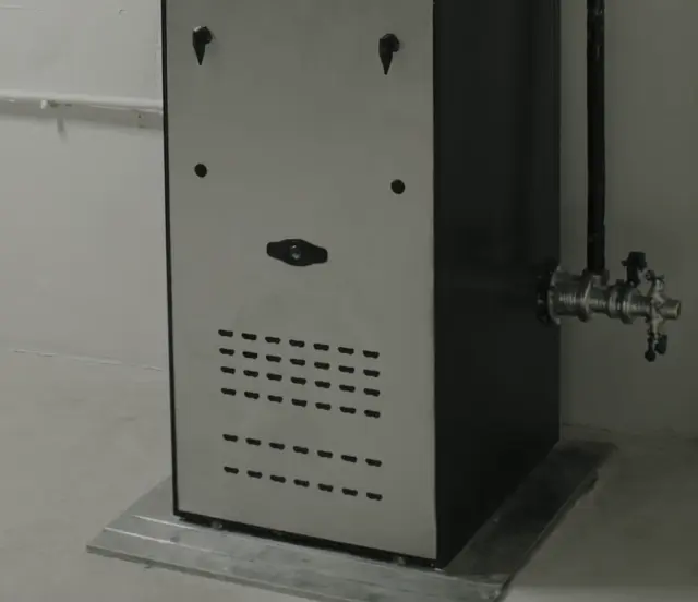 Brushed steel cabinet front with rows of louvers and two black handles, standing on a concrete floor